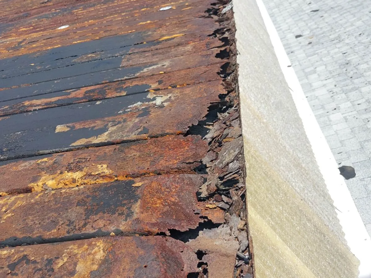 Deteriorated shingles along a rusted gutter and roof edge