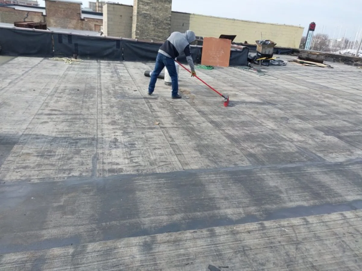 Roofer spreading adhesive on a commercial flat roof
